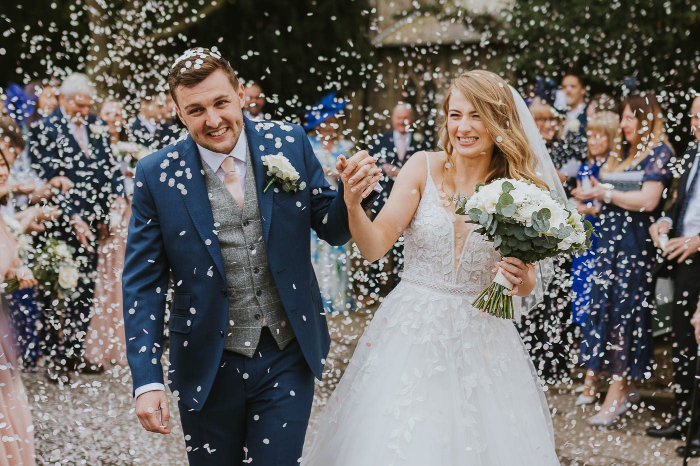 ripley castle wedding photography | photo of happy bride and groom walking through paper confetti after their church wedding ceremony at ripley castle